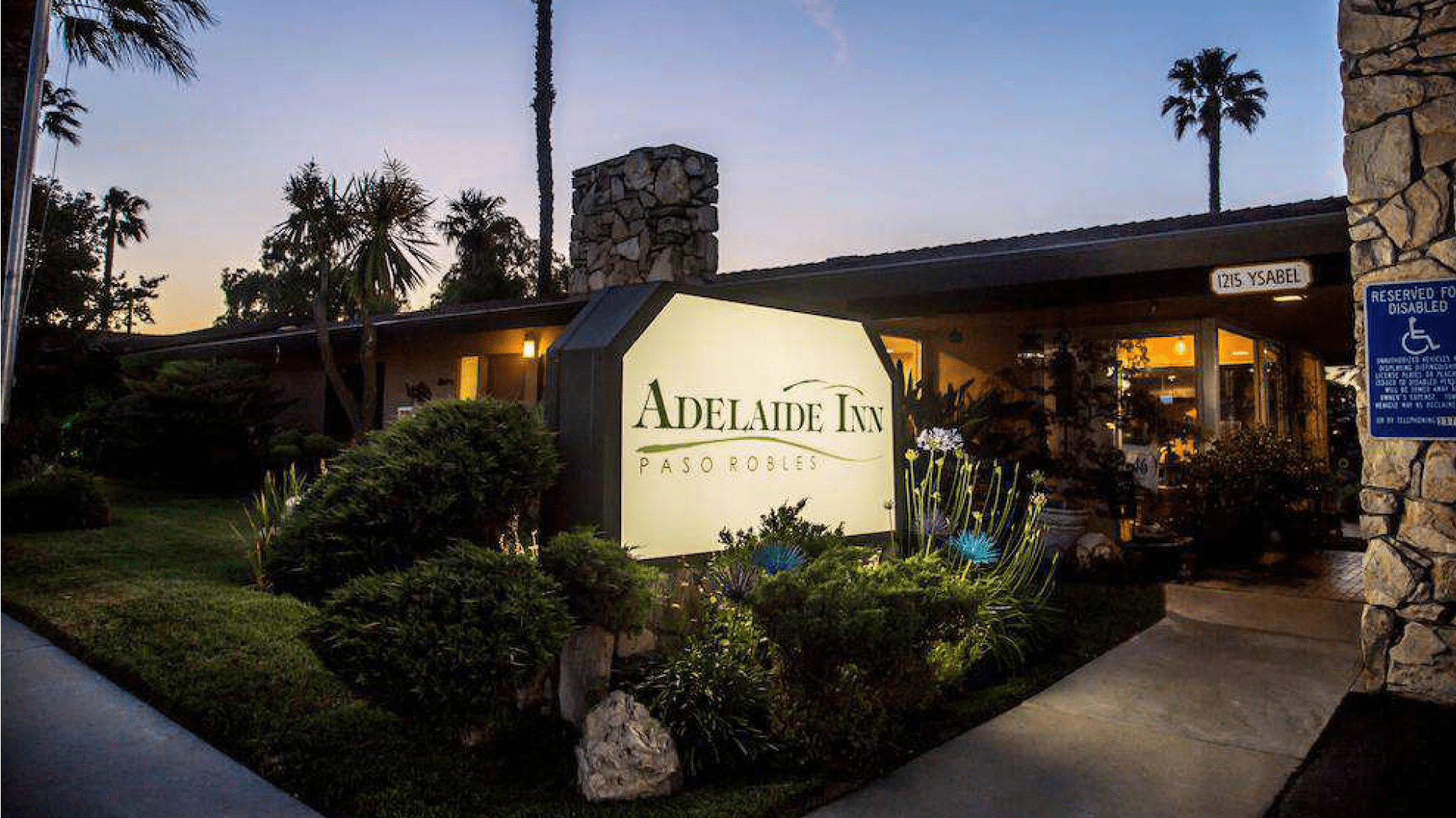 Illuminated sign for Adelaide Inn at dusk surrounded by greenery.